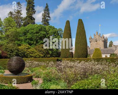 Giardino verde con siepi, piante e una scultura, sullo sfondo un castello di pietra sotto un cielo blu, inverness, Scozia, Gran Bretagna Foto Stock