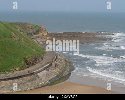 Un sentiero costiero lungo una scogliera rocciosa che scende fino alla spiaggia e al mare tempestoso, tynemouth, Inghilterra, Regno Unito Foto Stock