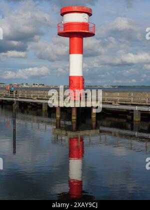 Faro in rosso e bianco al molo, che riflette sulle acque calme sotto un cielo parzialmente nuvoloso, Eckernfoerde, Schleswig-Holstein, Germania Foto Stock