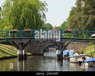 Ponte in legno sul canale, fiancheggiato da fiori, barche sull'acqua e alberi verdi sullo sfondo, friedrichstadt, schleswig-holstein, germania Foto Stock