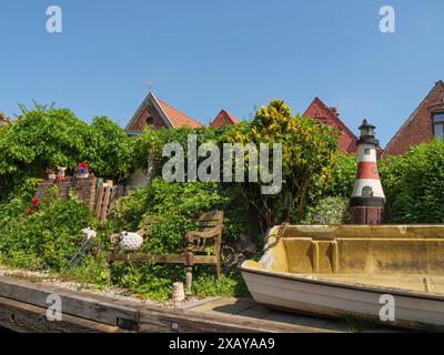 Un piccolo giardino con una panchina di legno, una barca e un piccolo faro di fronte alle case in un giorno d'estate, friedrichstadt, schleswig-holstein, germania Foto Stock