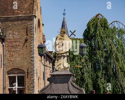 Vecchia statua di fronte a uno storico edificio in pietra con una chiesa sullo sfondo, Bruges, Belgio Foto Stock