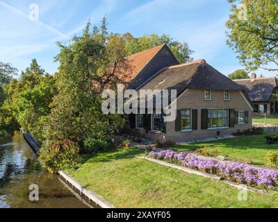 Casa accogliente con tetto in paglia e giardino ben tenuto sulla riva del fiume, circondata da vegetazione lussureggiante, giethoorn, Paesi Bassi Foto Stock