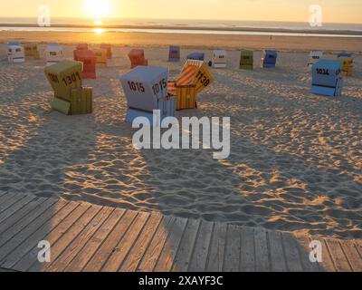 Sedie a sdraio sulla spiaggia al tramonto con una passeggiata in legno in primo piano, langeoog, germania Foto Stock