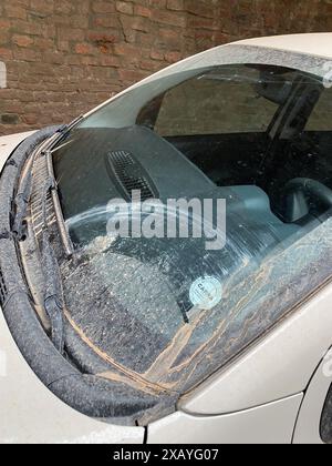 Cremona, Italia - 9 giugno 2024 l'auto d'argento parcheggiata su una strada cittadina è coperta da uno spesso strato di polvere dopo una tempesta di sabbia Foto Stock