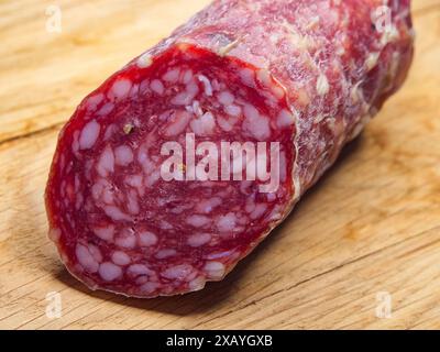 Un grosso pezzo di salsiccia affumicata su un tagliere di legno, colpo ravvicinato. Un'immagine appetitosa per gli amanti dei prodotti a base di carne, perfetta per le pubblicità gastronomiche Foto Stock