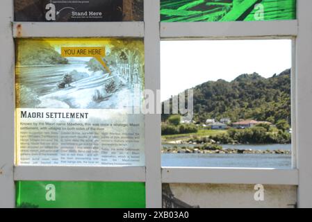 GREYMOUTH, NUOVA ZELANDA, 19 OTTOBRE 2023: La segnaletica turistica mostra una foto storica del Maori pa a Greymouth, mentre una finestra aperta rivela la scena di oggi oltre il fiume a Cobden. Foto Stock