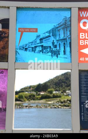 GREYMOUTH, NUOVA ZELANDA, 19 OTTOBRE 2023: La segnaletica turistica mostra una foto storica di Greymouth mentre una finestra aperta rivela la scena di oggi oltre il fiume a Cobden. Foto Stock