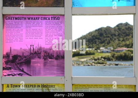 GREYMOUTH, NUOVA ZELANDA, 19 OTTOBRE 2023: La segnaletica turistica mostra una foto storica di Greymouth mentre una finestra aperta rivela la scena di oggi oltre il fiume a Cobden. Foto Stock