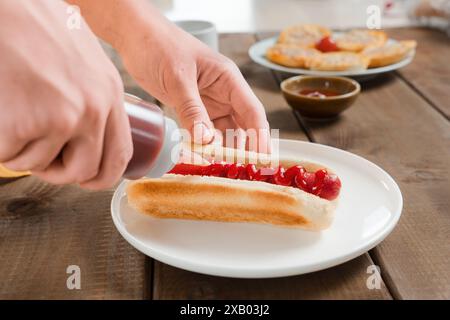 Una donna sprema il ketchup dalla bottiglia di ketchup a un hot dog, un fast food, un pranzo veloce o una colazione all'americana. Vegan o salsiccia di carne Foto Stock