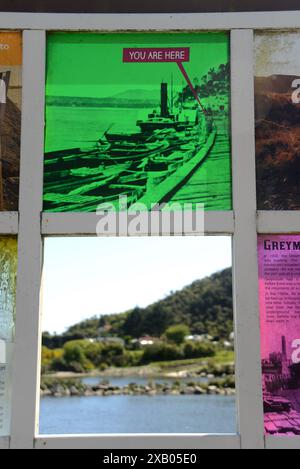 GREYMOUTH, NUOVA ZELANDA, 19 OTTOBRE 2023: La segnaletica turistica mostra una foto storica di Cobden mentre una finestra aperta rivela la scena di oggi. Foto Stock