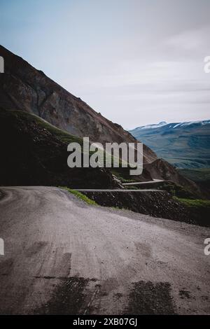 Scopri la bellezza selvaggia dell'Alaska con questa accattivante immagine di una tortuosa strada di montagna che mostra il terreno accidentato e il paesaggio sereno. Perfec Foto Stock