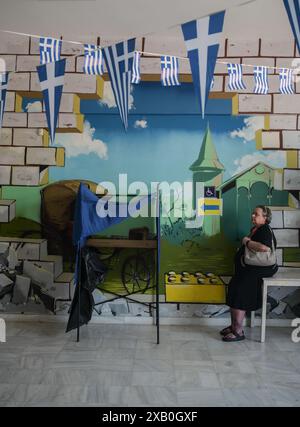 Atene, Grecia. 9 giugno 2024. Un votante si trova accanto a una cabina di votazione in un collegio elettorale decorato con bandiere greche. Gli elettori di 27 paesi dell'Unione europea si recano alle urne tra il 6 e il 9 giugno per eleggere i membri del Parlamento europeo. Crediti: Dimitris Aspiotis/Alamy Live News Foto Stock