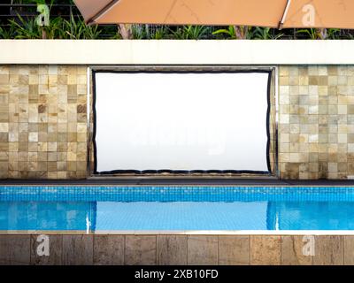 Grande schermo bianco bianco impermeabile per proiettore all'aperto appeso su piastrelle di sfondo accanto alla piscina. Proiezione film vuota a bordo piscina Foto Stock