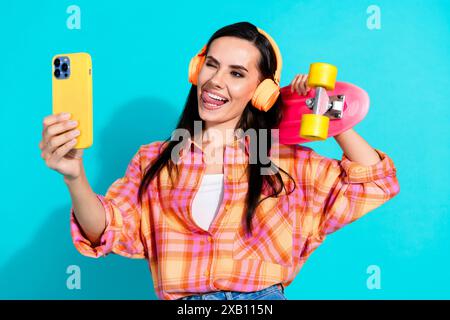 Foto ritratto di belle giovani donne cuffie skater selfie vestiti eleganti a quadri isolati su sfondo color acquamarina Foto Stock