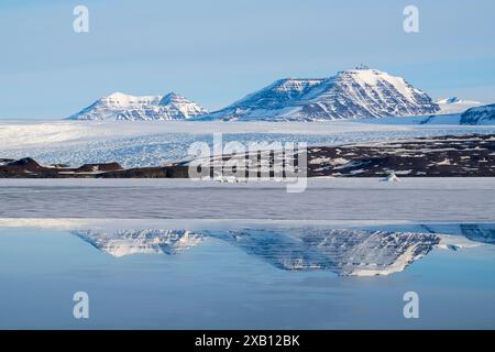 Groenlandia orientale, costa di Blosseville. I riflessi del fiordo ghiacciato di prima mattina con il ghiacciaio. Foto Stock