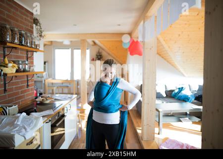 Madre che tiene in braccio il bambino piccolo, la mette in una fionda, avvolge. Amore paterno incondizionato, festa della mamma. Foto Stock