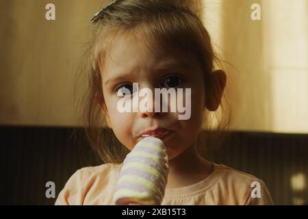 Un bambino carino è felice di gustare un delizioso gelato nella luce soffusa della luce naturale Foto Stock