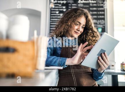 Donna proprietaria di un bar, barista che effettua ordini dal fornitore su tablet. Foto Stock