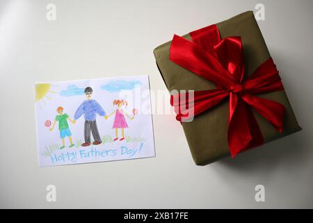 Festa del papà foto di una cartolina disegnata da un bambino. Un regalo di colore verde con un fiocco rosso. Sfondo bianco. La cartolina mostra un padre che cammina con ciao Foto Stock