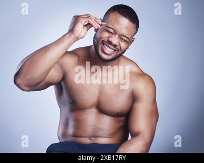 Uomo nero, pinzette e cura del corpo in studio, sicuro di sé e sopracciglia per l'epilazione su sfondo blu. Persona maschile, cura della pelle e manutenzione per l'igiene Foto Stock