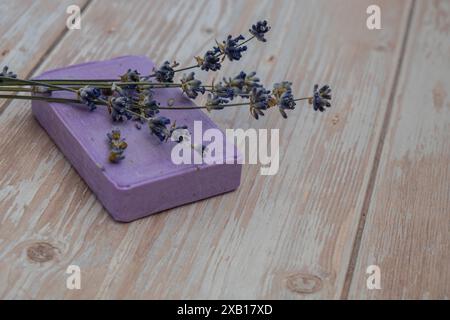 Sapone alla lavanda su sfondo di legno con spazio per la copia del testo. Mock-up del modello di annuncio. Prodotti cosmetici naturali fatti in casa per la cura della pelle. Fiore di lavanda secco biologico. Sapone fatto a mano Foto Stock