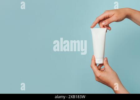 Due mani che tengono e aprono un tubo cosmetico bianco su uno sfondo azzurro Foto Stock