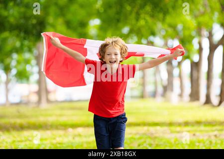 Bambino con bandiera canadese. Buon giorno del Canada. Bambino che corre con la bandiera nazionale che tira per il Canada in una partita di calcio o di hockey. Sostenitore canadese Foto Stock