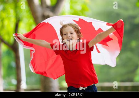 Bambino con bandiera canadese. Buon giorno del Canada. Bambino che corre con la bandiera nazionale che tira per il Canada in una partita di calcio o di hockey. Sostenitore canadese Foto Stock