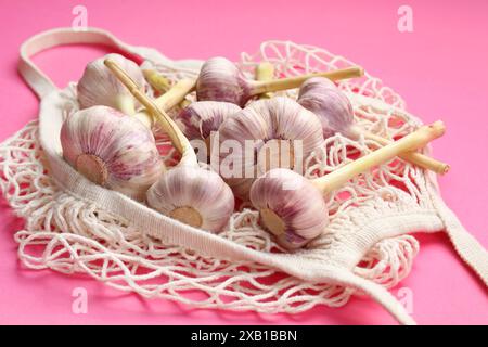 Borsa a cordoncino con teste d'aglio su sfondo rosa brillante, primo piano Foto Stock