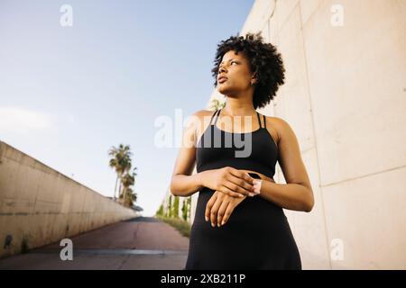 Donna che guarda in lontananza mentre è in piedi per strada prima di allenarsi. Giovane donna che indossa abiti sportivi per preparare il suo esercizio all'aperto Foto Stock