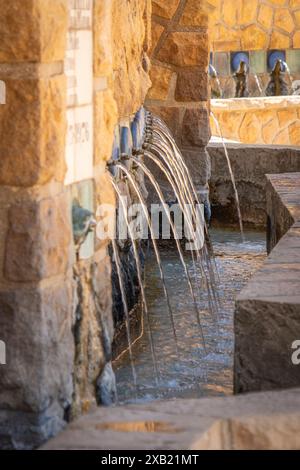 Una fontana rustica in pietra che presenta diversi ruscelli di acqua corrente in un ambiente sereno. Foto Stock