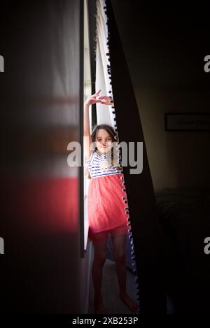 Bambina felice che balla dietro un sipario all'interno Foto Stock