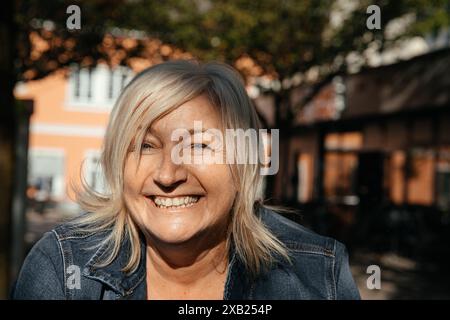 Donna più anziana con capelli biondi e un sorriso luminoso che si gode il sole Foto Stock