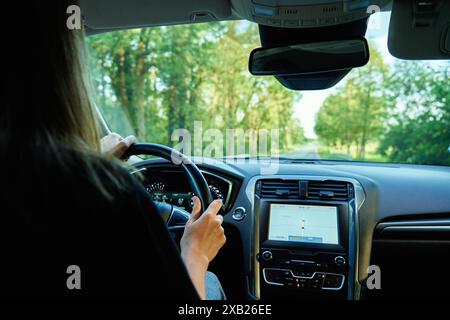 Donna che guida un'auto sulla strada di campagna al tramonto. Vista posteriore del conducente femminile nel veicolo Foto Stock