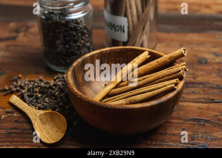 Cannella su una ciotola di legno e chiodi di garofano fuoriescono dal vaso di vetro delle spezie su un tavolo di legno, concetto di utilizzare spezie in cucina Foto Stock