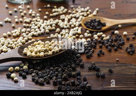 pepe nero e semi di pepe bianco su un cucchiaio di legno sopra un tavolo di legno Foto Stock