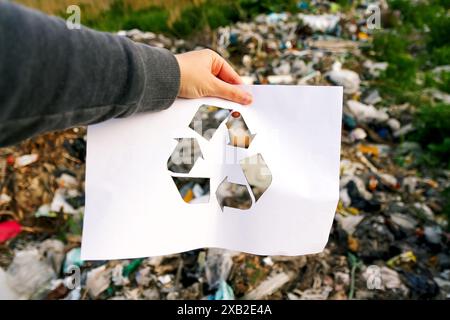 Mano che tiene il logo del riciclo sullo sfondo di un'immondizia. Adatto per campagne di sensibilizzazione ambientale. Foto Stock