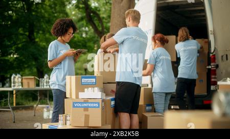 Gruppo di volontari che preparano donazioni di cibo gratuito e caricano pacchetti in un pulmino di carico in un giorno di sole. Gli operatori di beneficenza lavorano nell'organizzazione locale per gli aiuti umanitari. Foto Stock