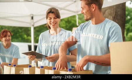 Gruppo felice di volontari che aiutano in una banca alimentare locale, preparano razioni gratuite di pasti a persone a basso reddito in un parco in una giornata di sole. Gli operatori di beneficenza lavorano nel Centro di donazione degli aiuti umanitari. Foto Stock