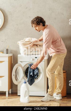 Un bell'uomo in intimi casalinghi si trova accanto a una lavatrice, pronto a pulire la sua casa. Foto Stock