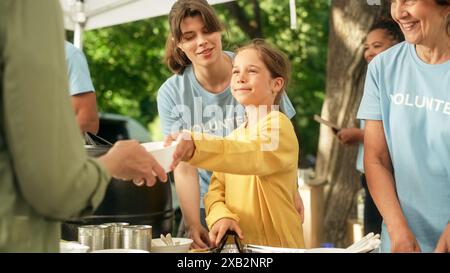 Amazing Young Girl Helping Volunteers in Humanitarian Aid Center, distribuendo cibo gratuito per la comunità locale bisognosa. Un team di lavoratori della beneficenza lavora a un evento all'aperto della Local Food Bank. Foto Stock