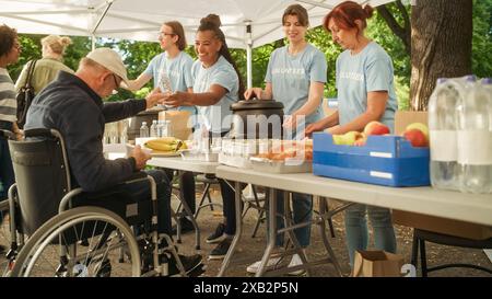 Uomo di mezza età felice con disabilità che utilizza la sedia a rotelle che riceve un pasto di beneficenza da una banca alimentare per gli aiuti umanitari. Volontari che aiutano le persone bisognose nella comunità locale. Foto Stock
