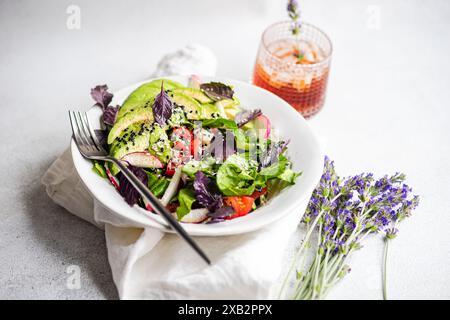 Un'insalata colorata di verdure fresche con lattuga, olive, pomodori ciliegini, cetrioli, ravanelli, e basilico rosso, cosparso di sesamo bianco e nero Foto Stock