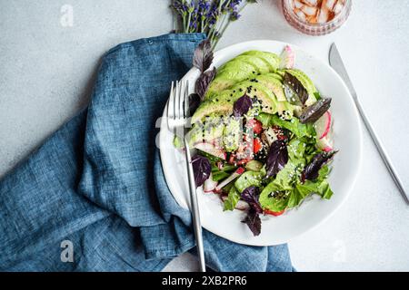 Insalata di verdure colorate con lattuga, olive, pomodori ciliegini, fette di cetriolo, ravanelli, basilico rosso, cosparso di semi di sesamo bianchi e neri Foto Stock