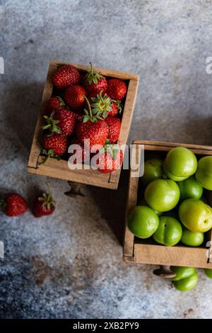 Scatole di legno vintage riempite con una selezione di fragole mature organiche, prugne verdi e ciliegie dolci su uno sfondo testurizzato Foto Stock