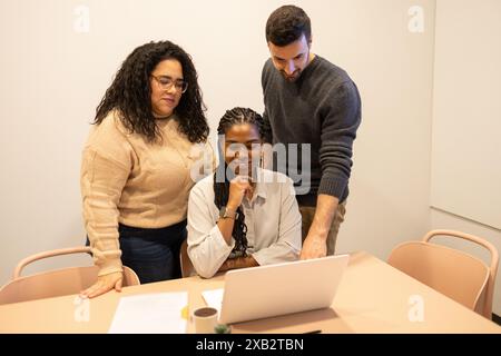 Un gruppo di tre amici o colleghi partecipa a una sessione di lavoro collaborativa in uno spazio di coworking, condividendo idee su un notebook Foto Stock