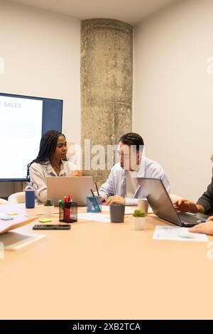 Team diversificato di giovani professionisti che collaborano a un tavolo in un moderno spazio di coworking con computer portatili e documenti Foto Stock