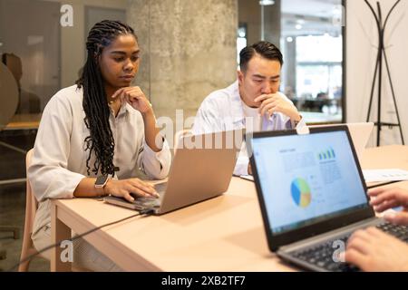 Due colleghi si sono impegnati nel lavoro, analizzando i dati sui notebook in un moderno ufficio di coworking con espressioni ponderate Foto Stock