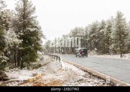 Una vista panoramica invernale di una strada nella Sierra De Guadarrama, caratterizzata da un'auto che viaggia tra la neve che cade dolcemente e alberi sempreverdi ricoperti di fresco Foto Stock